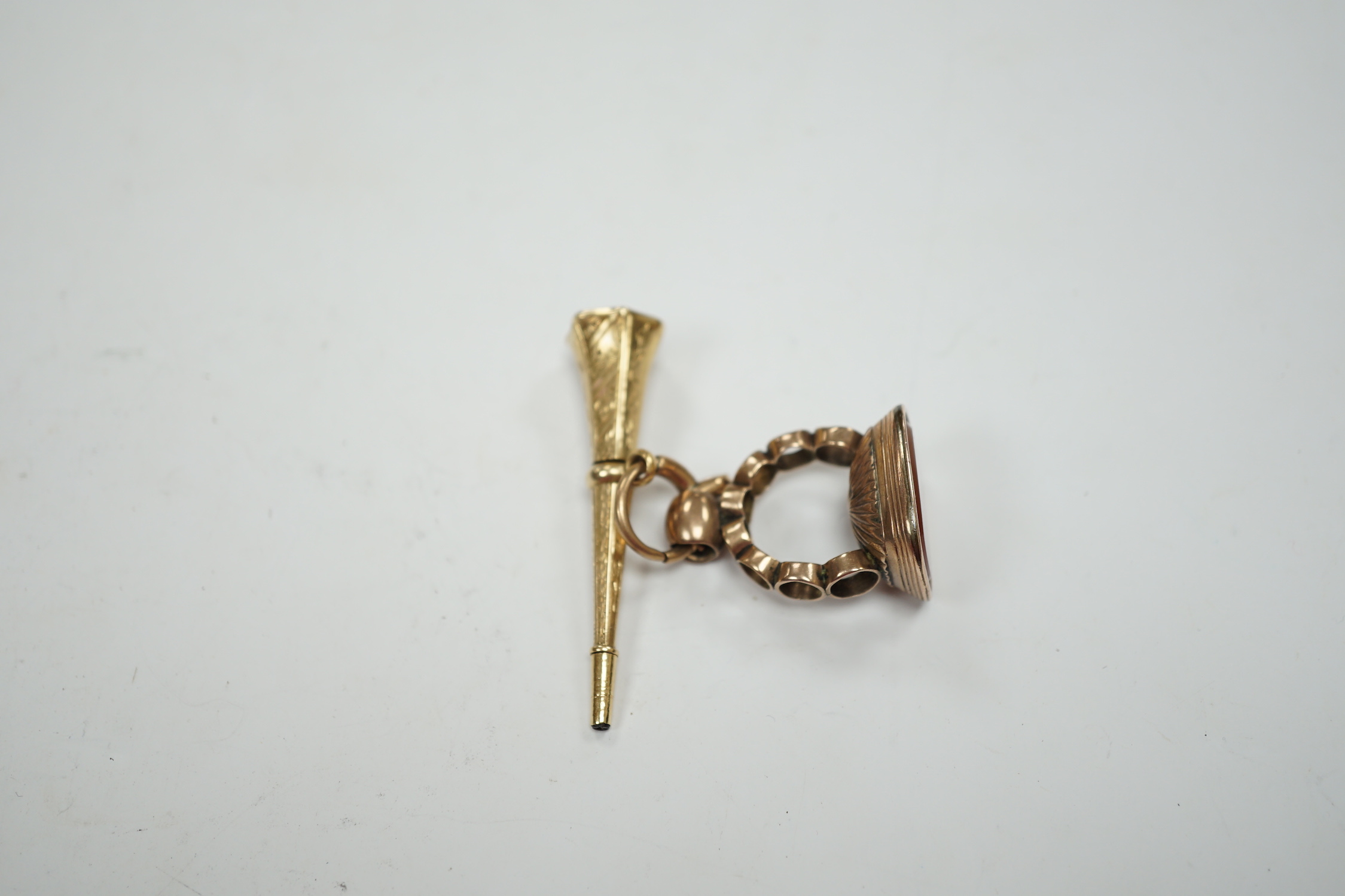 A 19th century engraved yellow metal overlaid and carnelian set trumpet shaped watch key, the matrix carved with crest and initial, 51mm, together with a 19th century gold plated and carnelian set fob.